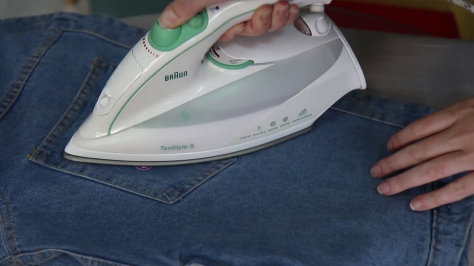 Девушка приклеивает заплатку на джинсы с помощью утюга