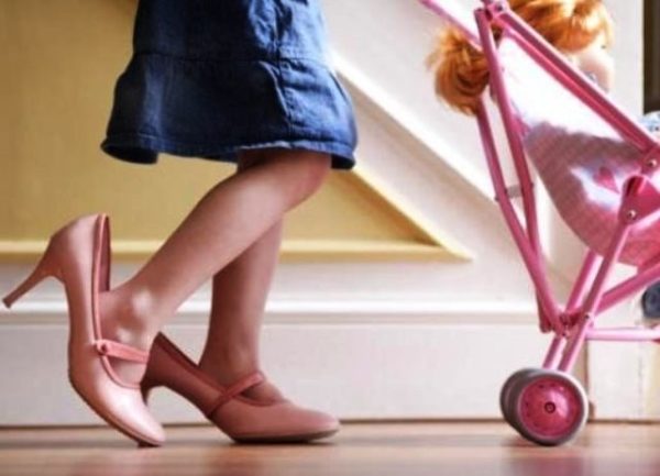 Девочка в больших розовых туфлях везёт игрушечную коляску