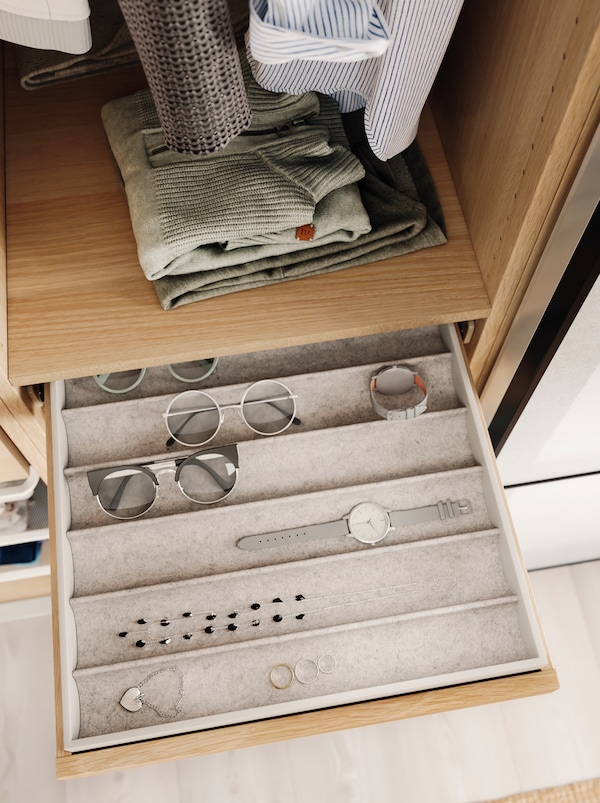 Очки, часы и украшения аккуратными рядами во вставке КОМПЛИМЕНТ в выдвижном ящике открытого гардероба.