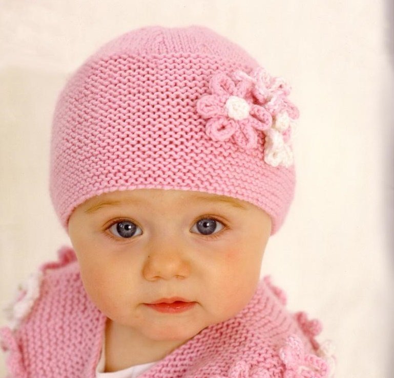 Розовая вязаная спицами шапка с цветком на маленькой девочке